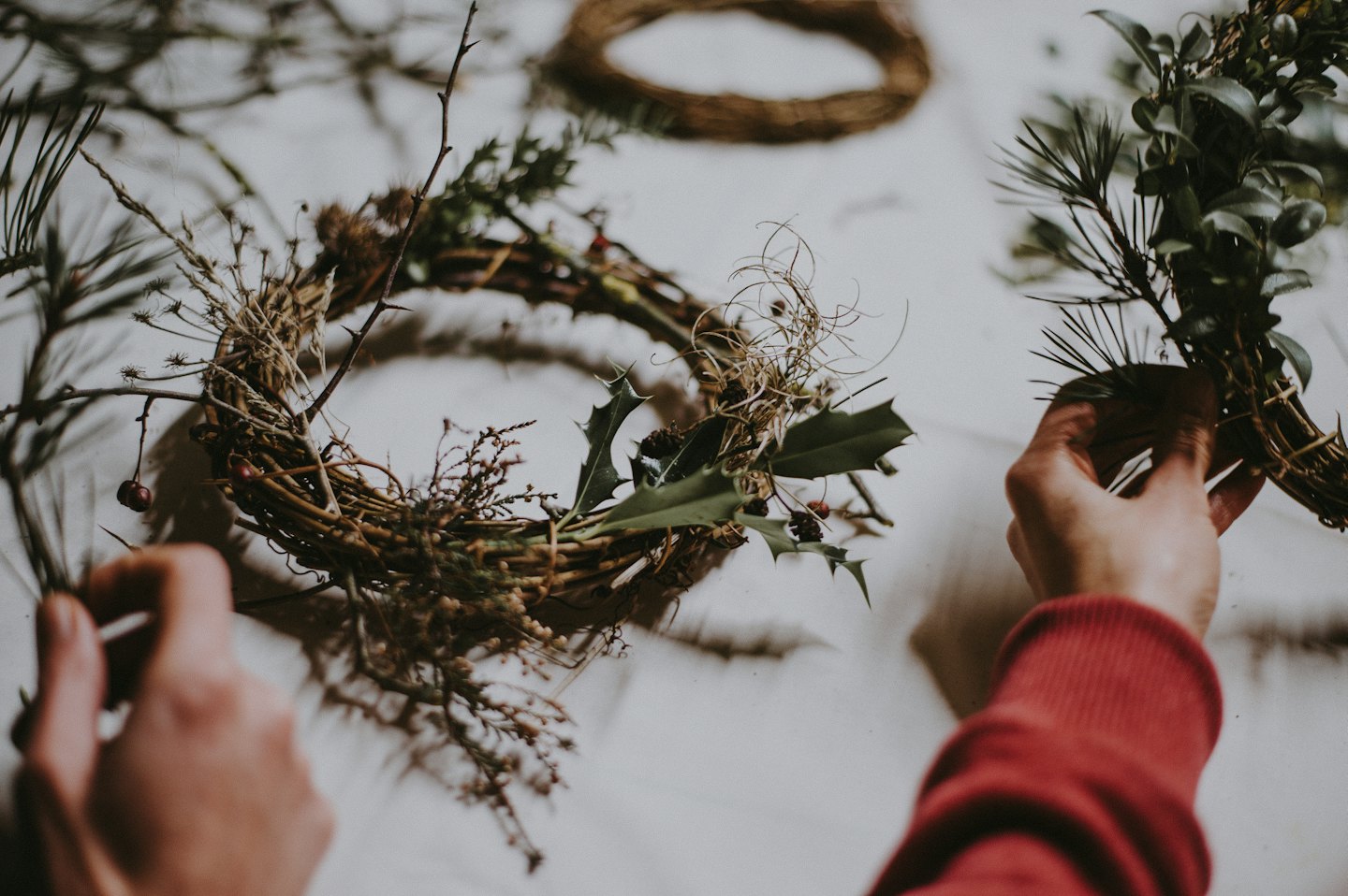 Hands arranging grapevine and evergreen sprigs into a natural wreath.