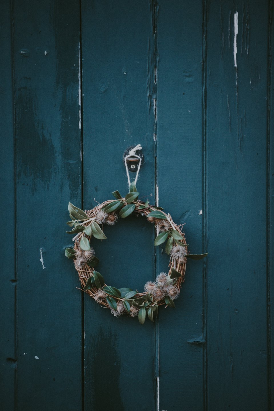 A rustic wreath hangs on a weathered teal wooden door.